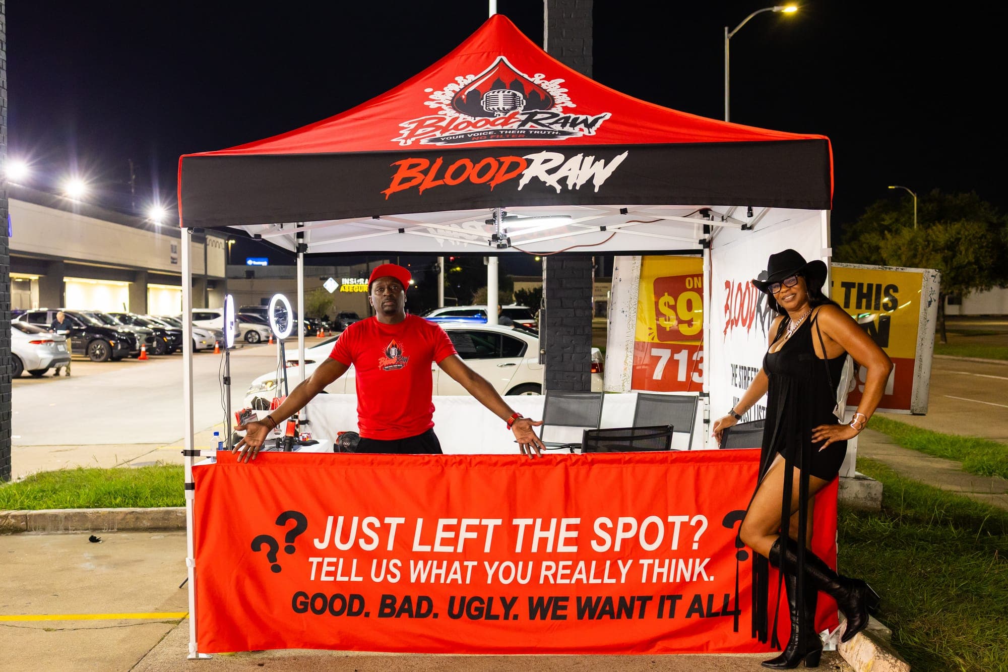 The BloodRaw pop-up tent at night, seen from the front, with a red banner reading 'Just left the spot? Tell us what you really think.'